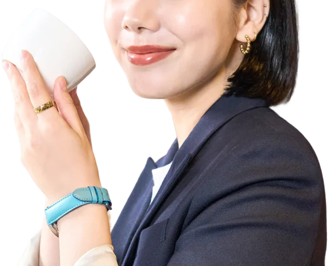 ターコイズの革ベルトの腕時計をつけ、カップを口元に運ぶ女性